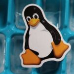 Close-up of a Linux penguin sticker placed on a blue ice cube tray with frozen cubes.