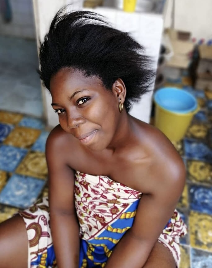 jeune femme noir en pagne les cheveux naturel assise sur un tabouret