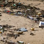 Plastic waste and debris littered across a sandy beach shore.